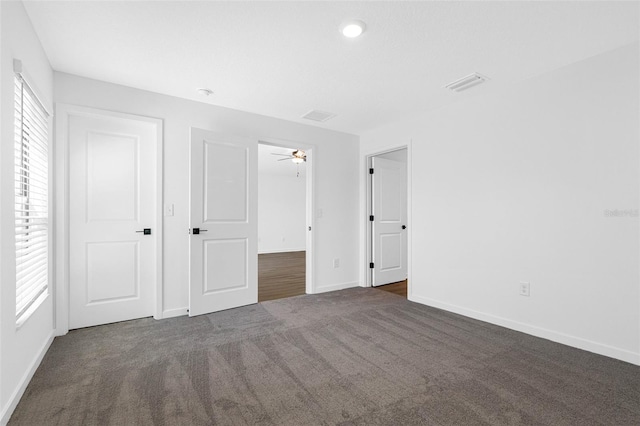 unfurnished bedroom featuring baseboards, visible vents, and dark carpet