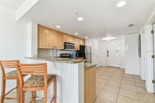 kitchen with light tile patterned floors, light stone countertops, visible vents, a peninsula, and stainless steel appliances