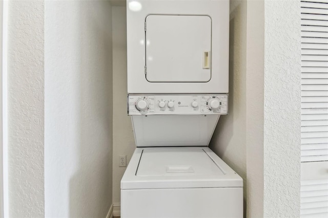 laundry area with a textured wall, laundry area, and stacked washing maching and dryer