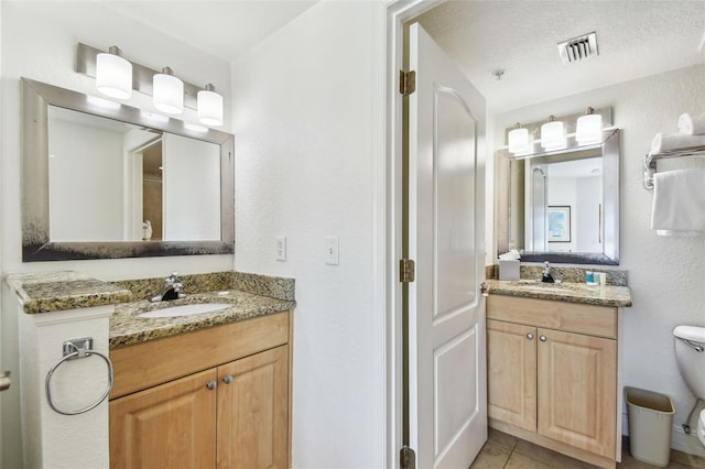 full bath featuring a sink, visible vents, toilet, and two vanities