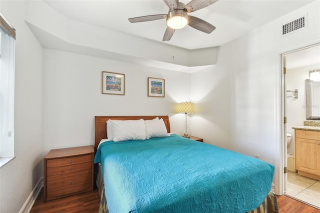 bedroom featuring a ceiling fan, baseboards, wood finished floors, visible vents, and connected bathroom