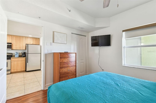 bedroom featuring light wood-style flooring, a closet, freestanding refrigerator, and ceiling fan