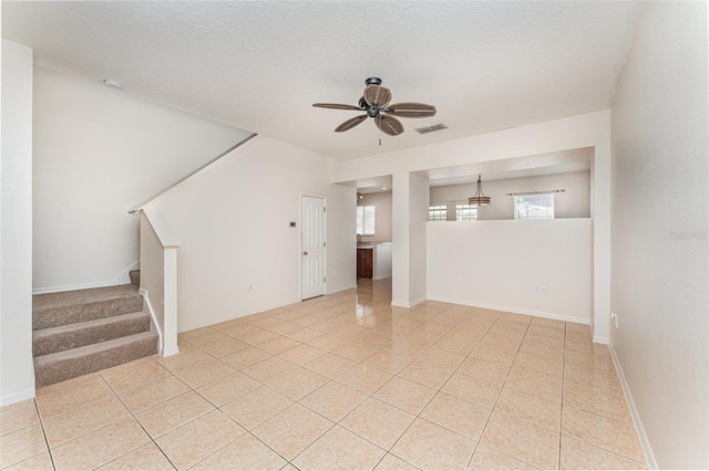 unfurnished living room with visible vents, a ceiling fan, stairway, light tile patterned floors, and baseboards