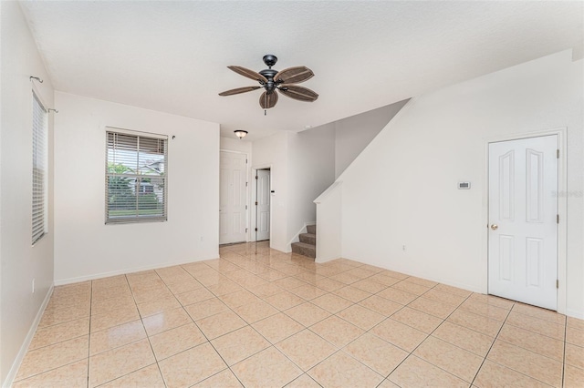 empty room with light tile patterned floors, stairway, and a ceiling fan