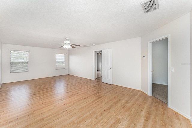 empty room with visible vents, baseboards, ceiling fan, light wood-type flooring, and a textured ceiling