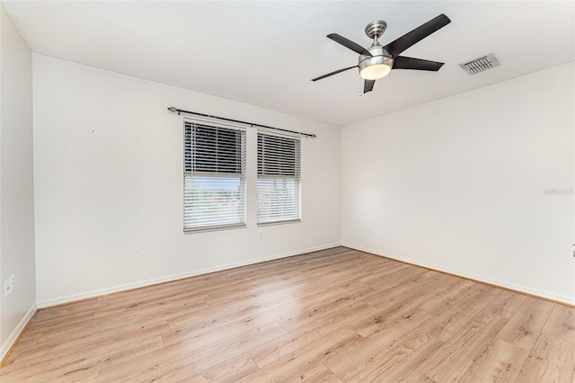 spare room featuring ceiling fan, light wood-style floors, visible vents, and baseboards