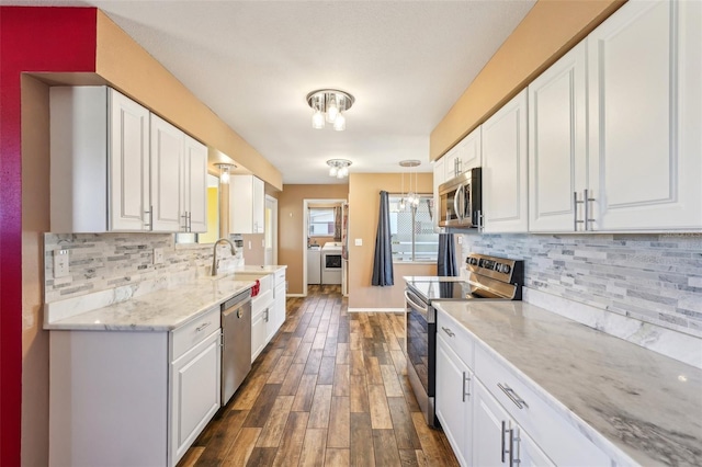 1021 Augusta Dr, Sun City Center, FL 33573 - kitchen with washing machine and clothes dryer, dark wood finished floors, a sink, stainless steel appliances, and white cabinetry