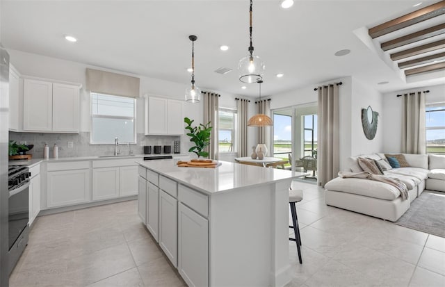 kitchen with a kitchen island, open floor plan, light countertops, decorative backsplash, and stainless steel gas range