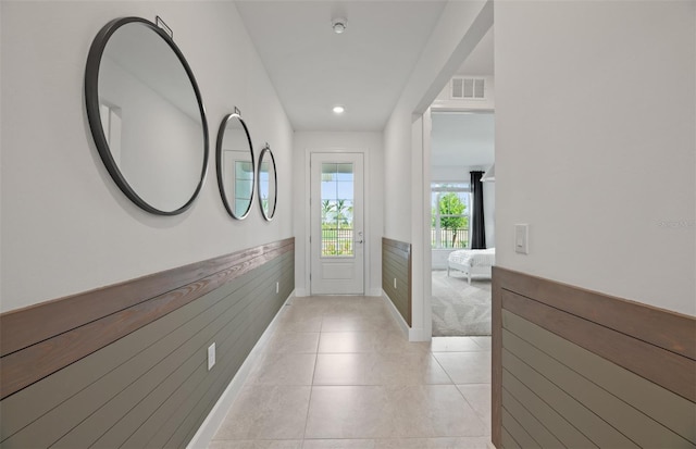 hall featuring wooden walls, light tile patterned floors, visible vents, and wainscoting