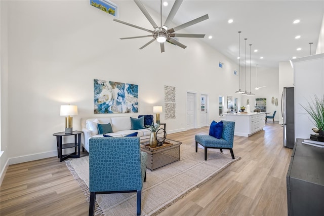 living area with light wood finished floors, baseboards, recessed lighting, a high ceiling, and a ceiling fan