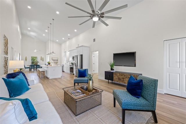 living area with a ceiling fan, visible vents, baseboards, light wood-style flooring, and a towering ceiling