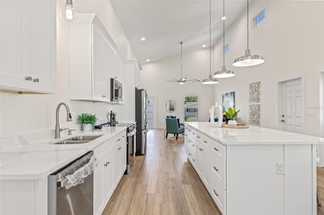 kitchen featuring light wood finished floors, ceiling fan, a sink, white cabinets, and appliances with stainless steel finishes