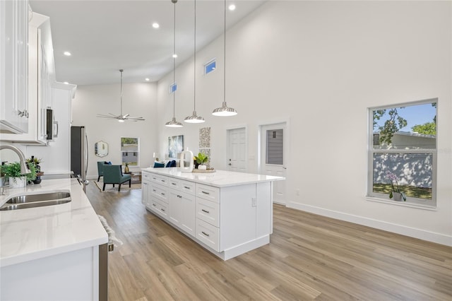 kitchen featuring light wood-style flooring, ceiling fan, a sink, white cabinets, and pendant lighting