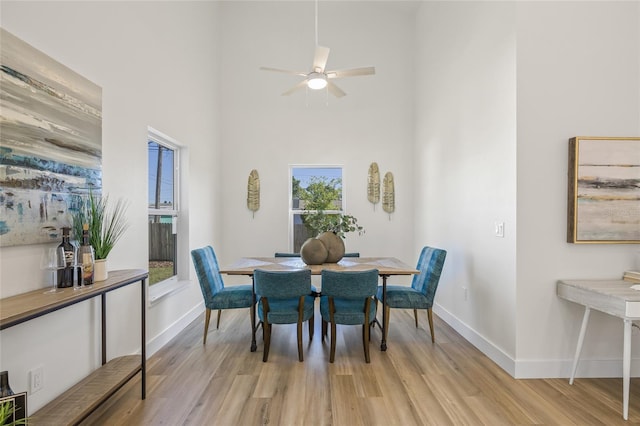 dining space with a high ceiling, baseboards, light wood finished floors, and ceiling fan