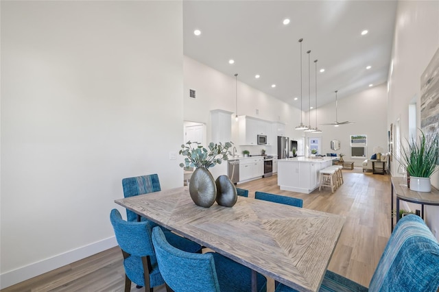 dining space with recessed lighting, light wood-style floors, a high ceiling, baseboards, and ceiling fan