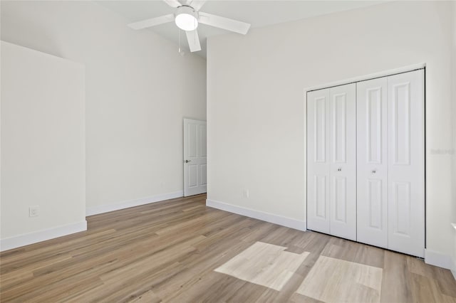 unfurnished bedroom featuring a high ceiling, wood finished floors, baseboards, and a closet