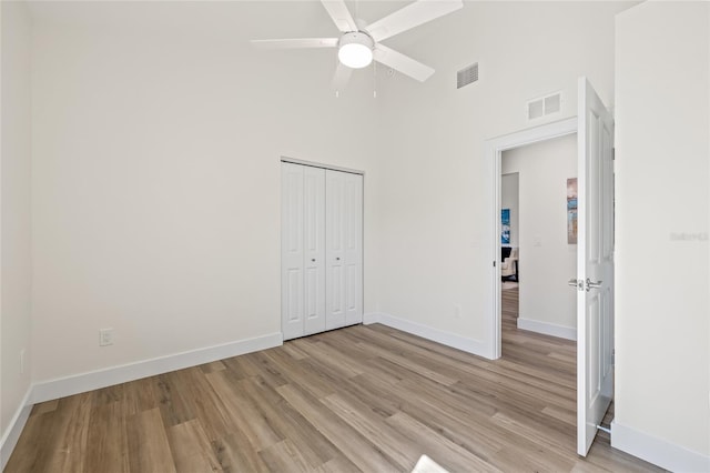 unfurnished bedroom featuring light wood-type flooring, visible vents, a closet, a high ceiling, and baseboards