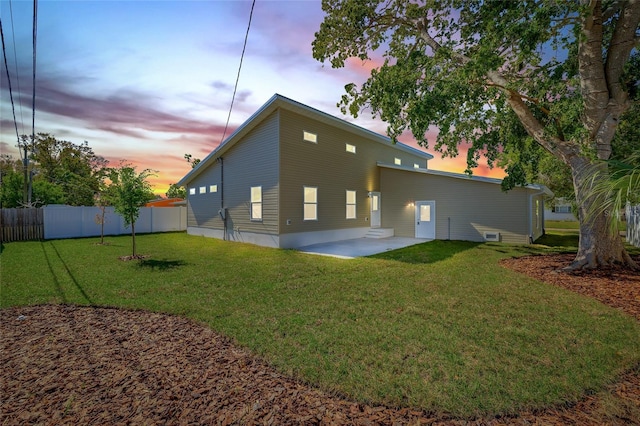 back of property at dusk featuring a patio area, a lawn, and fence