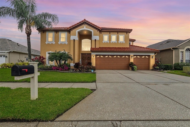 mediterranean / spanish home featuring stucco siding, a tiled roof, concrete driveway, and a yard