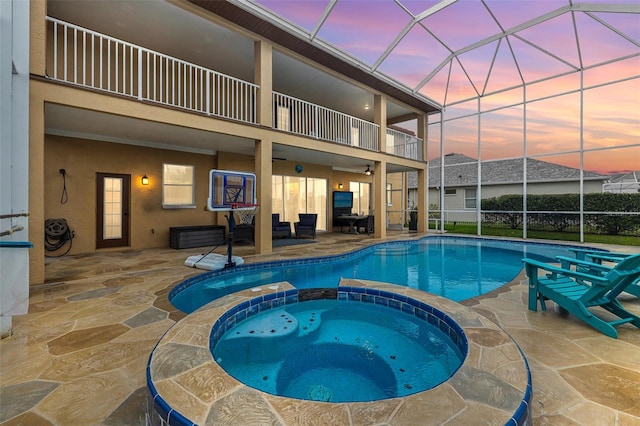 pool at dusk featuring a pool with connected hot tub, a lanai, and a patio area