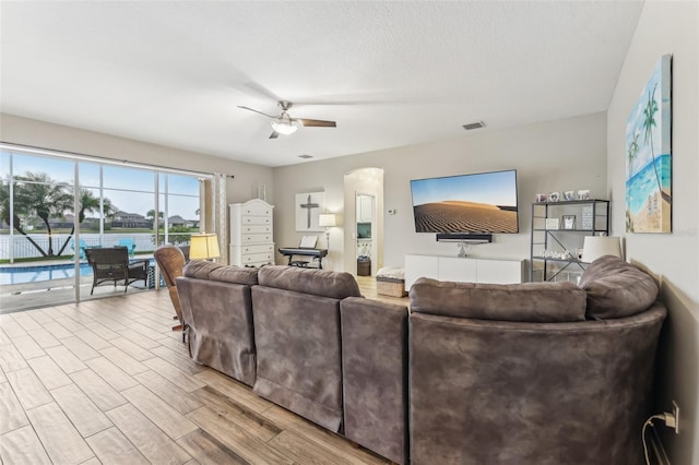 living area with wood finished floors, visible vents, arched walkways, ceiling fan, and a textured ceiling