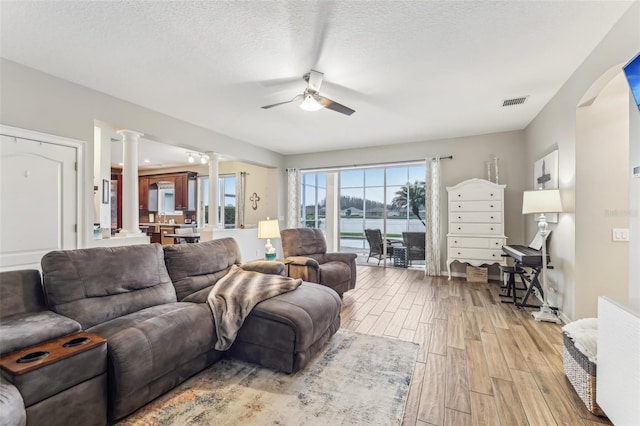 living area featuring a ceiling fan, visible vents, decorative columns, a textured ceiling, and light wood-type flooring