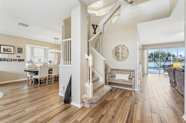 stairs featuring a chandelier, visible vents, baseboards, and wood finished floors