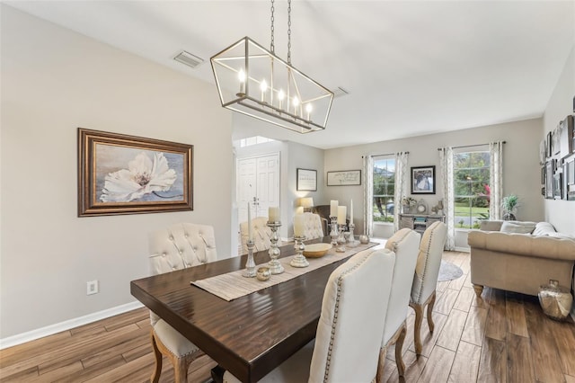 dining area featuring a notable chandelier, visible vents, baseboards, and wood finished floors