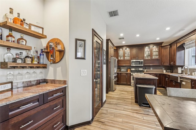 kitchen featuring light wood-style flooring, light stone countertops, appliances with stainless steel finishes, and a sink