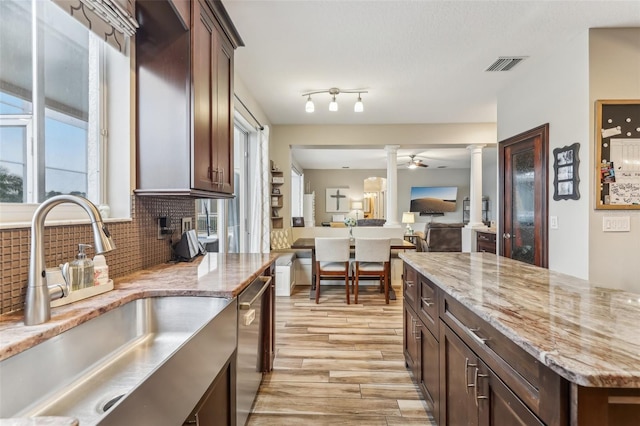 kitchen with light wood-type flooring, decorative backsplash, a sink, stainless steel dishwasher, and decorative columns