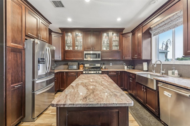 kitchen featuring visible vents, light stone counters, decorative backsplash, appliances with stainless steel finishes, and a sink