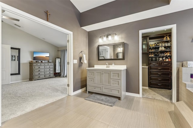 bathroom featuring vanity, baseboards, visible vents, vaulted ceiling, and a walk in closet