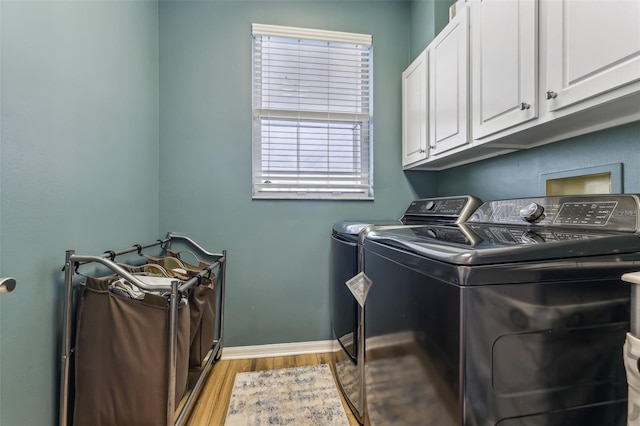 washroom featuring cabinet space, light wood-style flooring, washing machine and dryer, and baseboards