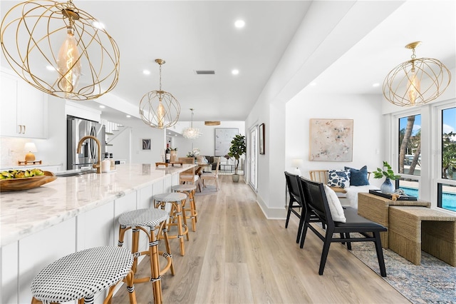 517 Belle Isle Ave, Belleair Beach, FL 33786 - kitchen with a chandelier, stainless steel fridge, light wood finished floors, white cabinetry, and a sink