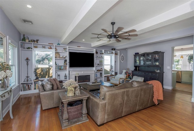 living area featuring a wealth of natural light, visible vents, beamed ceiling, and wood finished floors