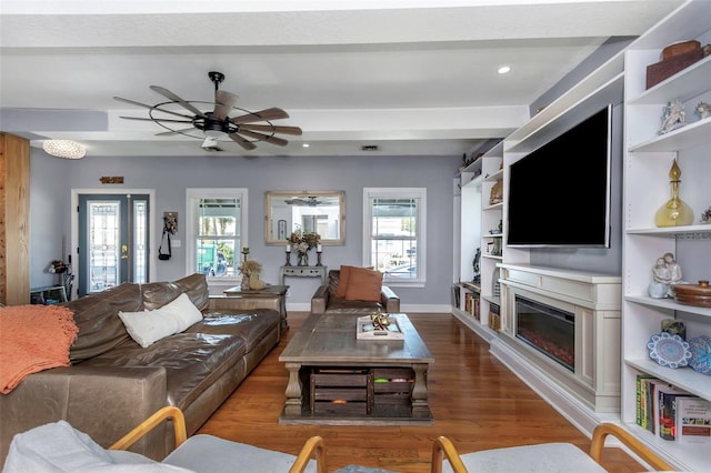 living room featuring a glass covered fireplace, wood finished floors, recessed lighting, baseboards, and ceiling fan