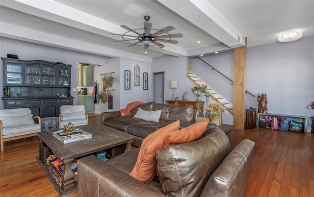 living area featuring stairway, beamed ceiling, a ceiling fan, and hardwood / wood-style flooring