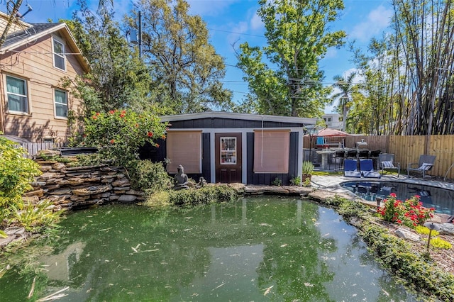 view of outbuilding featuring a garden pond, an outdoor structure, and fence