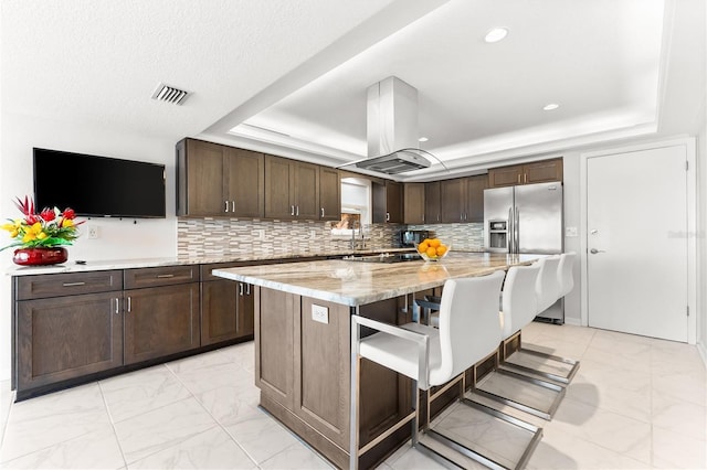 520 Belle Isle Ave, Belleair Beach, FL 33786 - kitchen with visible vents, a tray ceiling, stainless steel fridge, island range hood, and dark brown cabinets