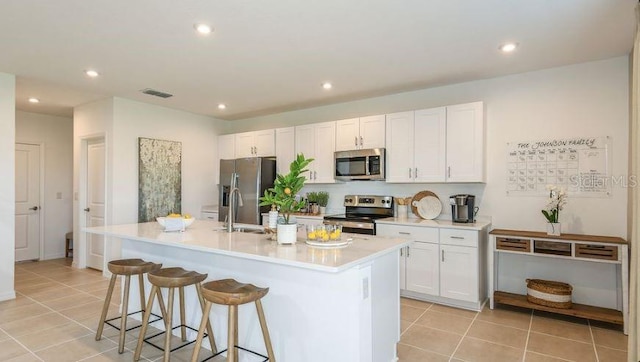 kitchen featuring visible vents, a breakfast bar, a kitchen island with sink, a sink, and appliances with stainless steel finishes