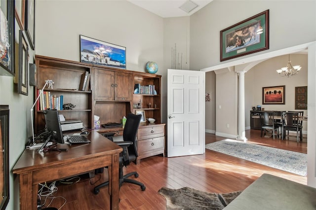 office featuring wood finished floors, baseboards, an inviting chandelier, a high ceiling, and decorative columns