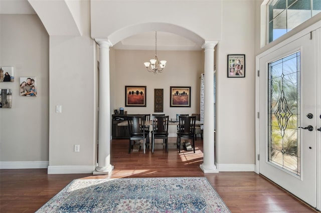 foyer entrance with a notable chandelier, decorative columns, wood finished floors, and a wealth of natural light