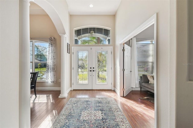 entryway with decorative columns, french doors, a towering ceiling, wood finished floors, and arched walkways