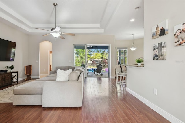 living area with dark wood-style floors, arched walkways, baseboards, and ceiling fan