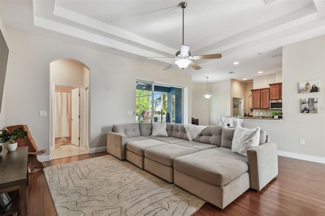 living room featuring arched walkways, baseboards, a tray ceiling, and wood finished floors