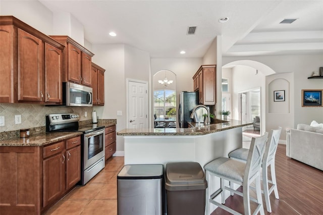 kitchen with visible vents, a kitchen bar, arched walkways, appliances with stainless steel finishes, and decorative backsplash