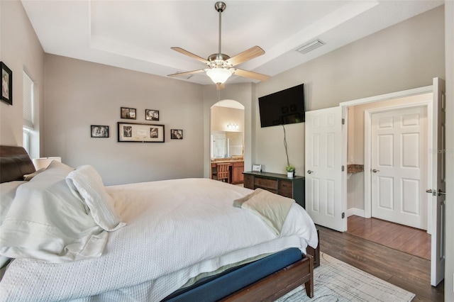 bedroom featuring a ceiling fan, visible vents, arched walkways, dark wood-style flooring, and a raised ceiling