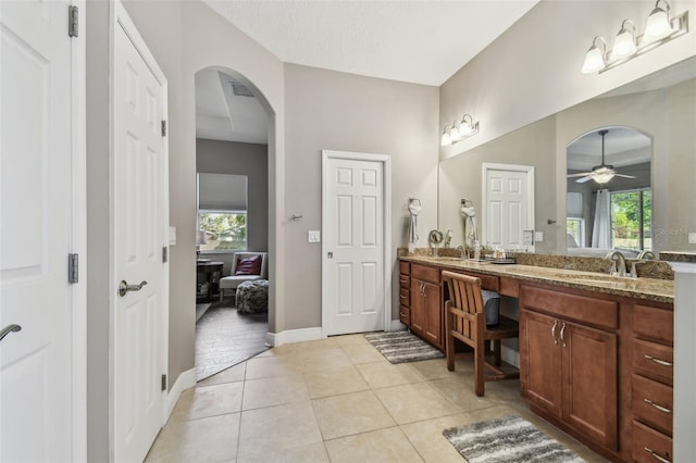 ensuite bathroom featuring tile patterned floors, plenty of natural light, a ceiling fan, and a sink