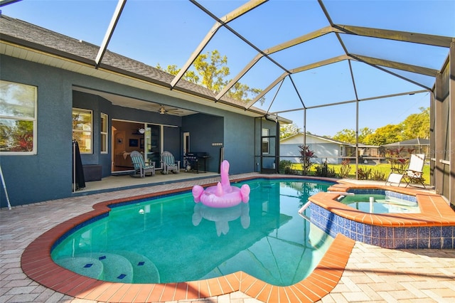 view of pool featuring glass enclosure, a pool with connected hot tub, a ceiling fan, and a patio area