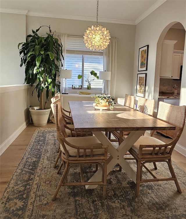 dining area with light wood-style flooring, baseboards, arched walkways, and ornamental molding